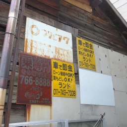 マルフク看板「電話の金融・販売 元町」。その右下にも真っ白になったマルフク看板がある。