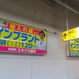 武蔵関エキナカ歯科の看板が横に2枚並んでいる。「総入れ歯からインプラント」「武蔵関エキナカ歯科 インプラント」